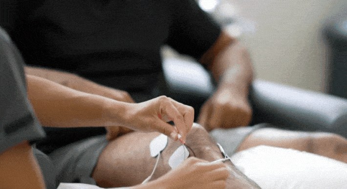 Fisioterapista che applica gli elettrodi per l'elettrostimolazione sul ginocchio di un paziente